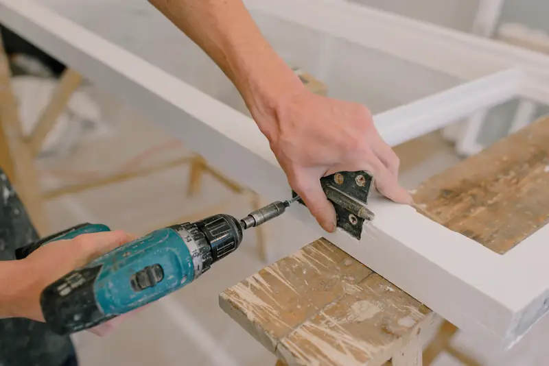 A cordless drill driving a hinge screw into a white cabinet door frame