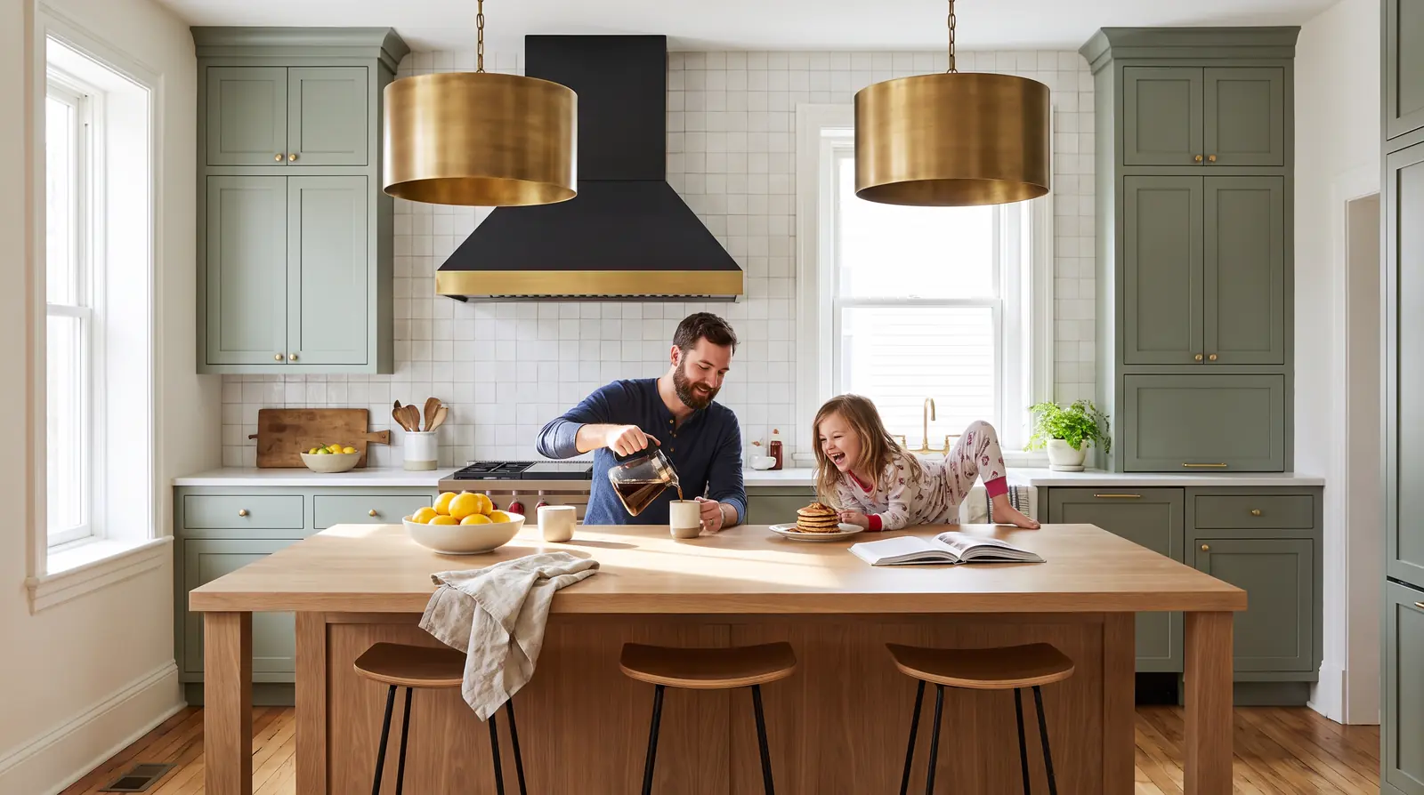 A dad pours coffee while his daughter laughs over pancakes at the white oak island of their finished sage kitchen